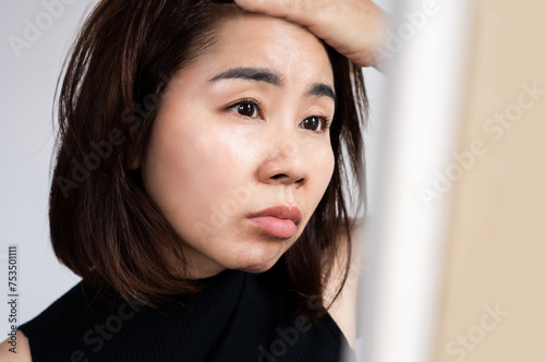 worried Asian woman have problem with oily skin on t zone of her face looking in a mirror