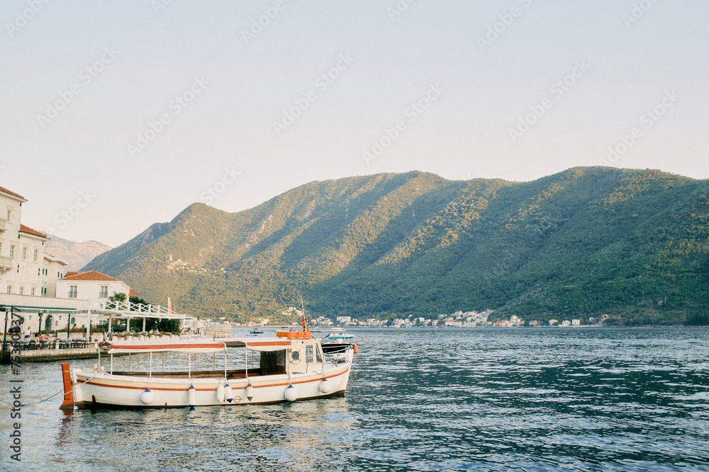 Tour boat is moored near the promenade with covered open-air restaurants. Perast, Montenegro