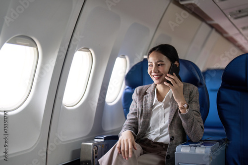 Asian young businesswoman successful or female entrepreneur in formal suit in a plane sit in a business class seat and uses a smartphone during flight. Traveling and Business concept © Natee Meepian