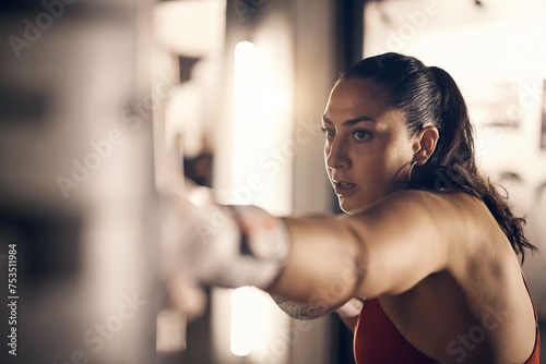 Fit young woman wearing a tank top and boxing gloves hitting a punching bag hanging in a gym during a boxing practice session photo