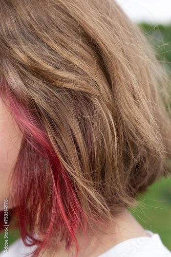 Close-up of the abundant hair of a teenage girl with light brown hair, blonde highlights and red dyed highlights in the outside. Concept of hair coloring, highlights and haircut. Beauty and fashion