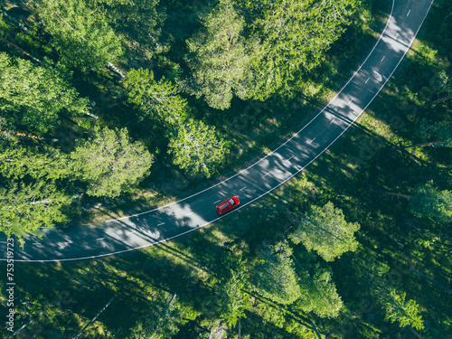 Aerial view of red car with a roof rack on a country road and green woods in Finland