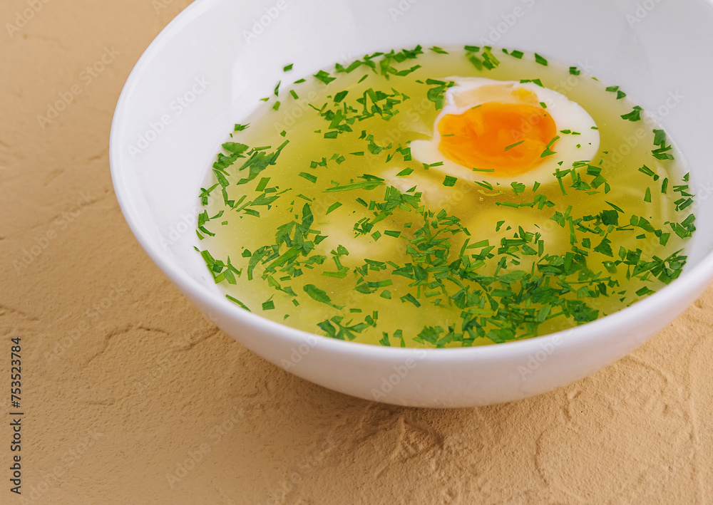 Chicken soup with egg and dill in white bowl