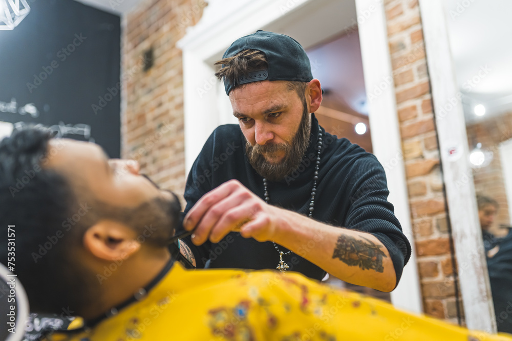 Focused barber trimming facial hair of his Indian client in a modern barbershop. High quality photo Focused barber trimming facial hair of his Indian client in a modern barbershop. High quality photo
