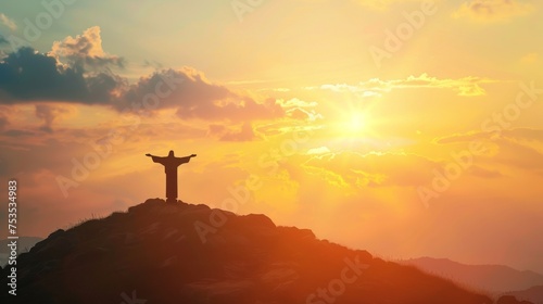 Jesus Christ silhouette with open arms atop a mountain during sunrise. © furyon