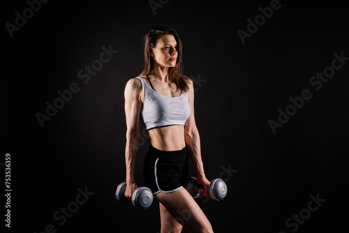 Sporty female doing exercise with dumbbells, silhouette studio shot dark yellow background
