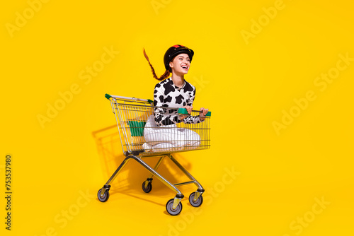 Full size profile portrait of overjoyed girl inside market pushcart ride empty space isolated on yellow color background