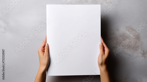 Top view of Woman's hand gracefully holding a blank white magazine on a gray background, serving as a design template mockup. © sema_srinouljan