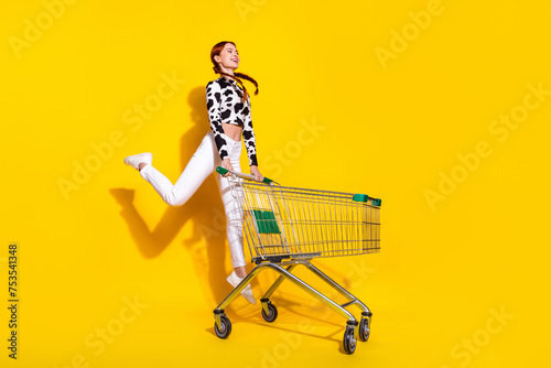 Full body portrait of energetic charming girl jump hold hypermarket trolley isolated on yellow color background