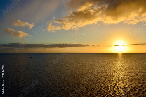 Golden sunset at sea  sailing boat on horizon  reflections of sunrays  sunset sky with clouds