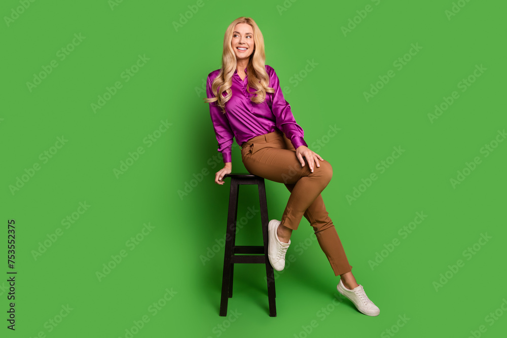 Naklejka premium Full length photo of positive thoughtful woman wear violet shirt sitting bar stool looking empty space isolated green color background