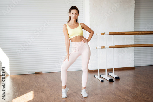 Confident woman in a yellow top and pink leggings posing in a dance studio.