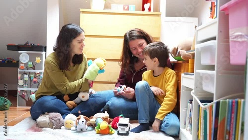 LGBTIA+ family of two mothers and their son playing with puppets together on the floor in the room photo