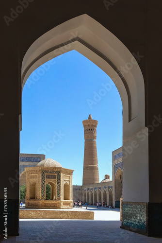 Bukhara, Uzbekistan. Archway frames minaret of Kalon mosque against blue sky, intricate Islamic design, mausoleum. Cover page