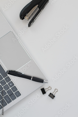 A silver laptop with a black pen, a black stapler on an office desk, top view.