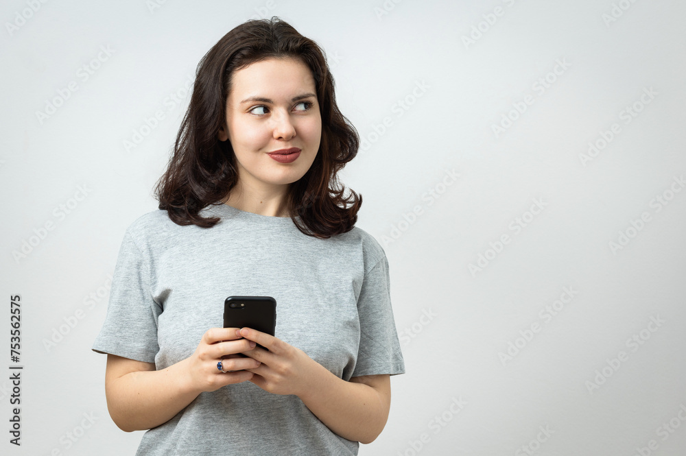 Cheerful beautiful young girl holding a cellphone and looking away, copy space, isolated on gray background Cheerful beautiful young girl holding a cellphone and looking away, copy space, isolated on gray background