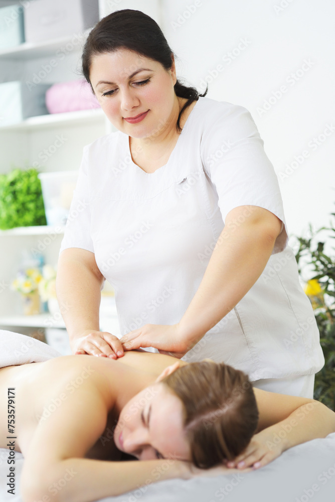 masseur massages the back, lower back, shoulders and neck of a young woman against the background of a bright office and greenery. masseur massages the back, lower back, shoulders and neck of a young woman against the background of a bright office and greenery.