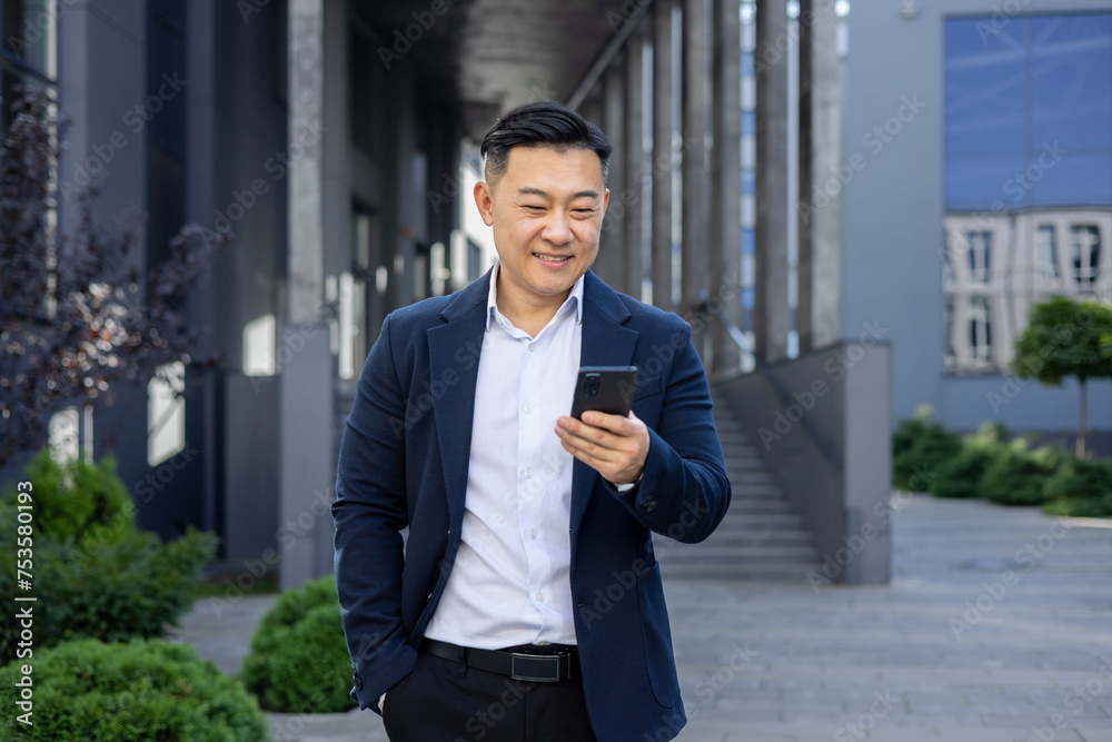Smiling asian businessman using smartphone outdoors in modern urban setting
