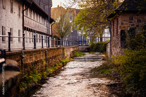 Fototapeta Naklejka Na Ścianę i Meble -  A serene creek flows through an old town, its waters glistening at dusk, flanked by traditional half-timbered houses and a cobblestone path