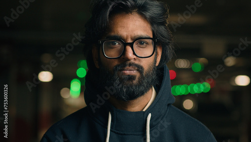 Male portrait outdoors in city town dark night underground serious confident calm Arabian man Indian Muslim guy at parking lot looking at camera bearded millennial driver in glasses ethnic hipster