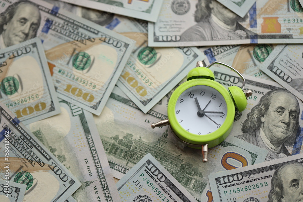 Alarm clock on hundred dollar bills banknotes. Background of time management, business and deadline concept Alarm clock on hundred dollar bills banknotes. Background of time management, business and deadline concept