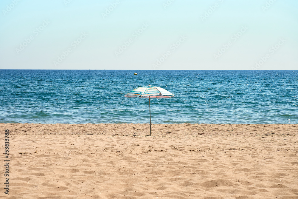 Lonely beach umbrella on the sand. Minimalist seascape. Beach and rest.