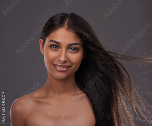 Hair care, wind and portrait of happy woman with beauty, shine and skincare isolated on a gray studio background. Hairstyle, cosmetics and face of Indian model in salon with makeup at hairdresser