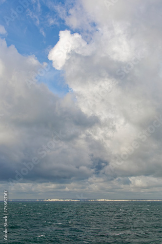 The White Cliffs of Dover as a Vessel transits through the Straits of Dover in the English Channel  with billowing white and dark clouds onshore.