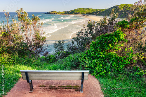 A bench on top of a cliff overlooking the Australian coast with a sandy beach. View from the cliff on a sunny summer day.