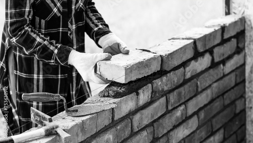 A young female builds a wall, puts a brick on a cement mortar