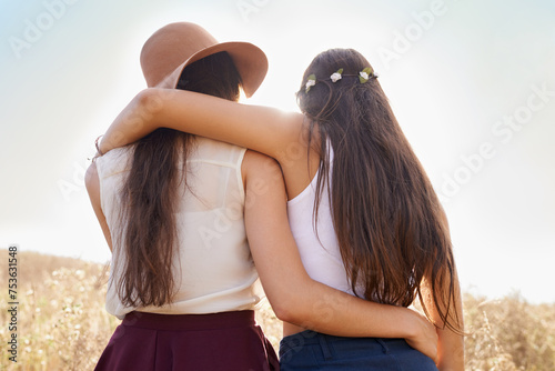 Friends, hug and walking on path in nature on holiday or journey on vacation in summer for adventure. Women, hiking or relax outdoor together on trail in woods, trekking on hill or travel environment photo