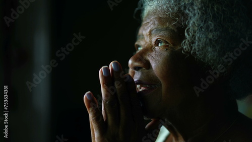 Faithful and Spiritual Senior African American woman with gray hair opening eyes feeling GRATEFUL while PRAYING to GOD. One religious elderly lady in 80s close-up face