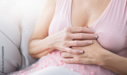 A woman is sitting on a couch with her hands on her chest. She is wearing a pink shirt and has a baby bump. Concept of comfort and relaxation  as the woman is at ease in her home environment