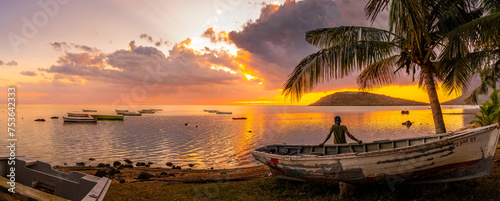 View of local man sat on boat viewing Le Morne from Le Morne Brabant at sunset, Savanne District, Mauritius