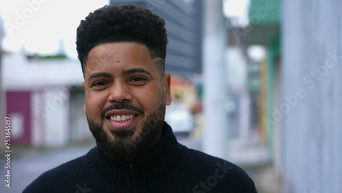 One happy young black Brazilian man walking in city street forward toward camera smiling. 20s South American person in urban environment portrait