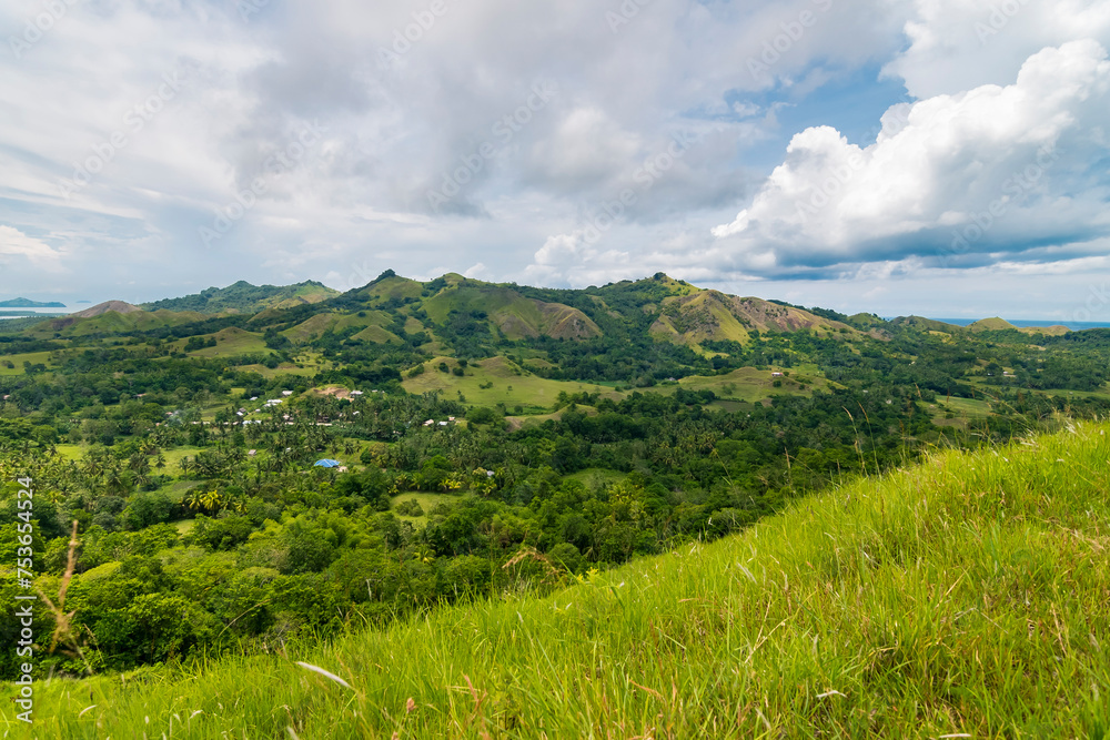 A picturesque view of Mabini, Bohol featuring rolling green hills, tropical vegetation, and a serene sky.