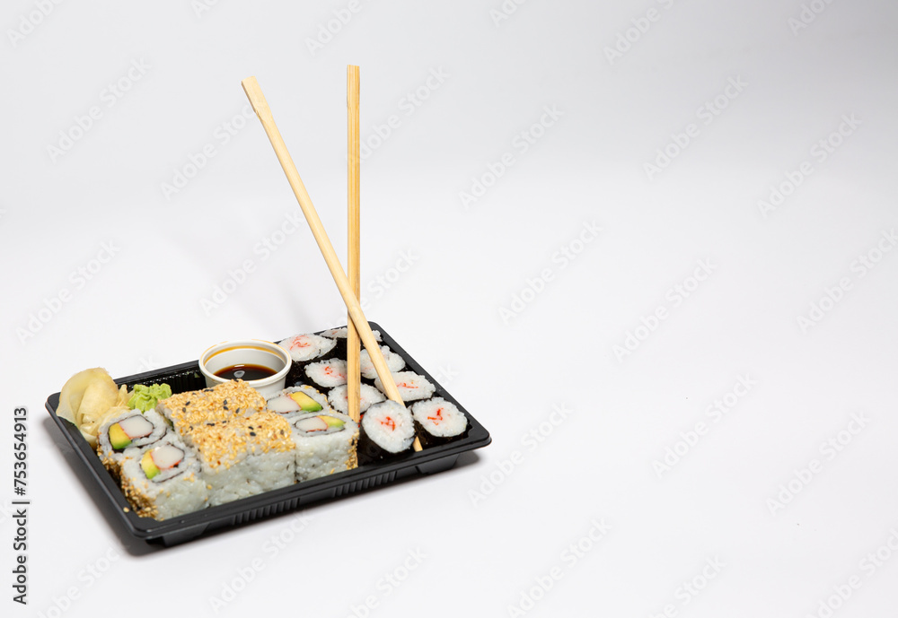 Sushi to go in a black takeaway box with wooden chopsticks on white background Sushi to go in a black takeaway box with wooden chopsticks on white background