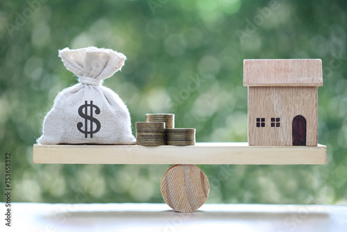 Model house and money bag on wood scale seesaw on natural green background, Business investment and real estate concept photo