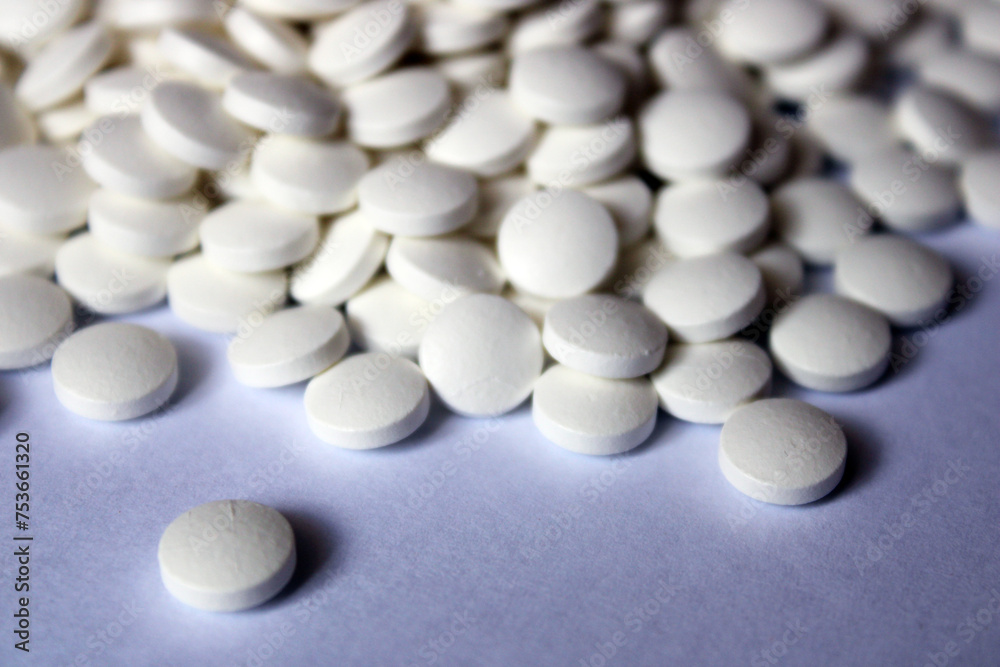 A lot of white pills are scattered on a white background. A lot of white pills are scattered on a white background.