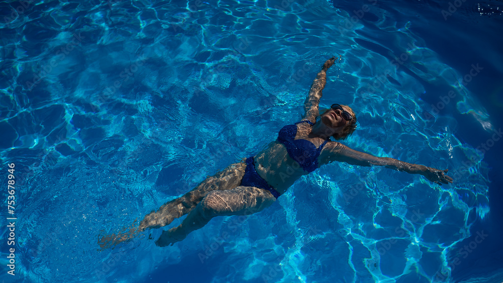 An elderly woman in sunglasses swims on her back in the pool. Vacation in retirement. 