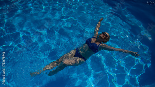 An elderly woman in sunglasses swims on her back in the pool. Vacation in retirement. 