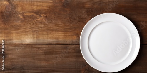 Overhead view of empty white circle plate on wooden table with napkin.