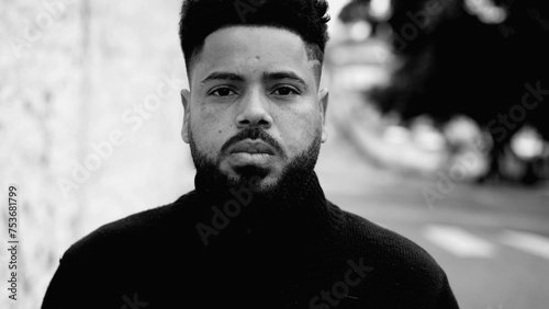 One serious young black man walking forward in urban street with stern serious expression. 20s South American person feeling confident in black and white, monochromatic