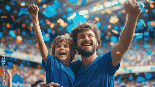 An excited father and son in blue shirts cheer for their favorite team during a football match. Football concept © Petrova-Apostolova