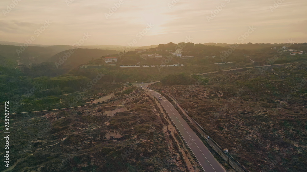 Beautiful sunset road passing green valley aerial view. Straight asphalt roadway