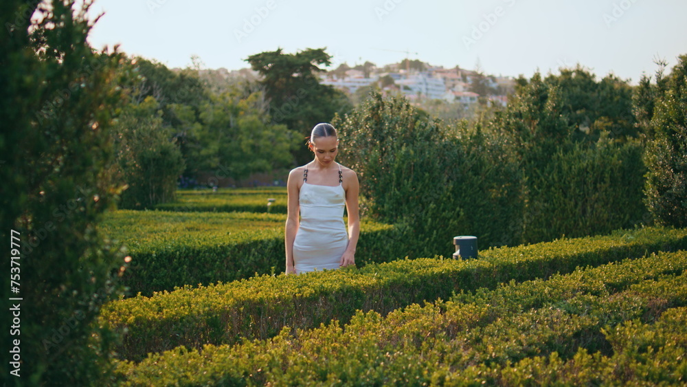 Dreamy woman touching bushes in green park. Romantic girl standing in garden