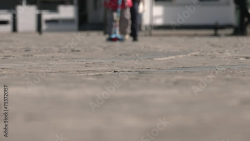 city ​​life on a sunny spring day, a woman strolls along the city square with her daughter on a scooter. close-up of legs of people walking with a scooter. smooth refocusing from the paving to legs photo