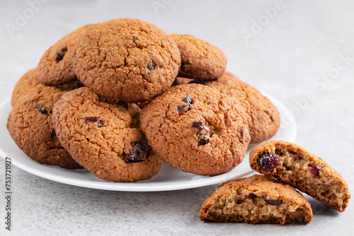 On a light background on a plate there are oatmeal cookies with dried cranberries.