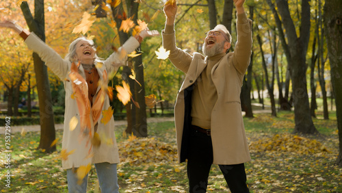 Happy carefree old Caucasian couple love retired woman and man throwing yellow leaves in autumn park forest together enjoy fallen leafage funny mature senior male female cheer playing rejoice laugh