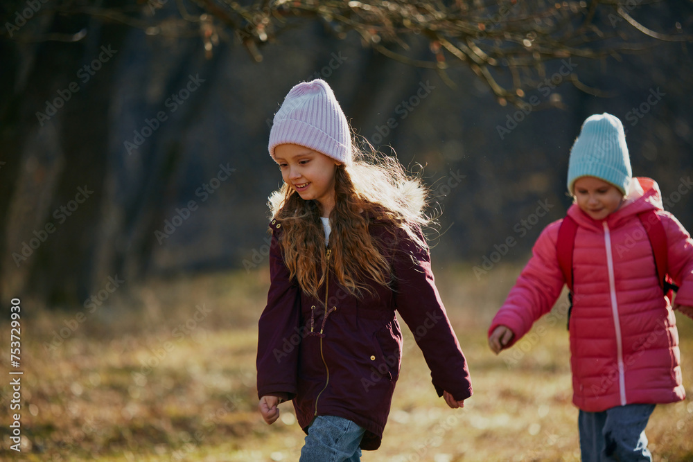 Kids, schoolgirls in colorful winter attire playfully walking along trail in countryside. Environment lesson. Concept of outdoor activities for children's development, school, childhood, fashion. Ad Kids, schoolgirls in colorful winter attire playfully walking along trail in countryside. Environment lesson. Concept of outdoor activities for children's development, school, childhood, fashion. Ad